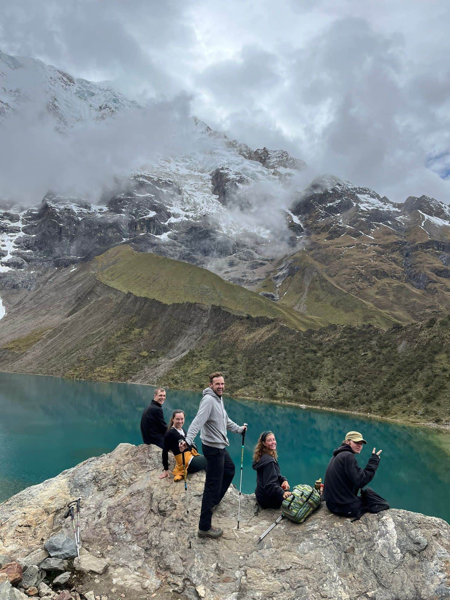 Konex group resting on a rock above a glacial lake below a snow-capped peak