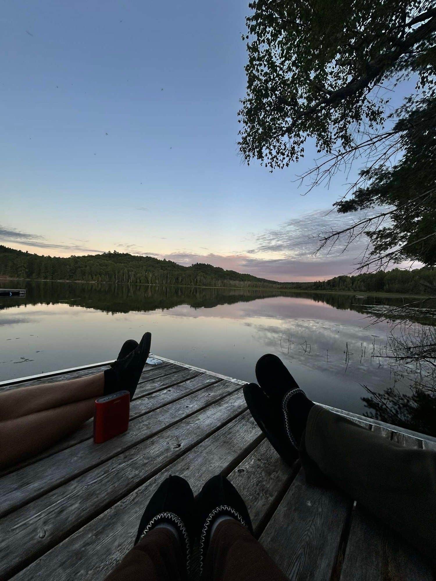 Feet up on a wooden dock looking across a still lake at dusk